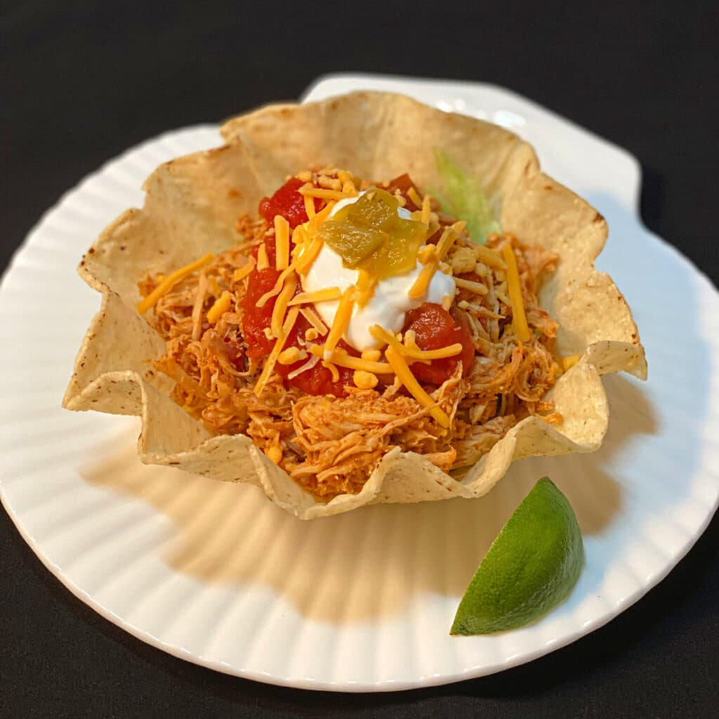 Side view of shredded chicken in a taco shell topped with sour cream, shredded cheese and salsa