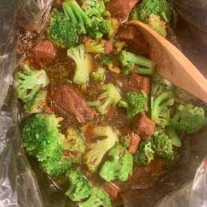Top view of green broccoli and meat chunks being stirred by a wooden sppon
