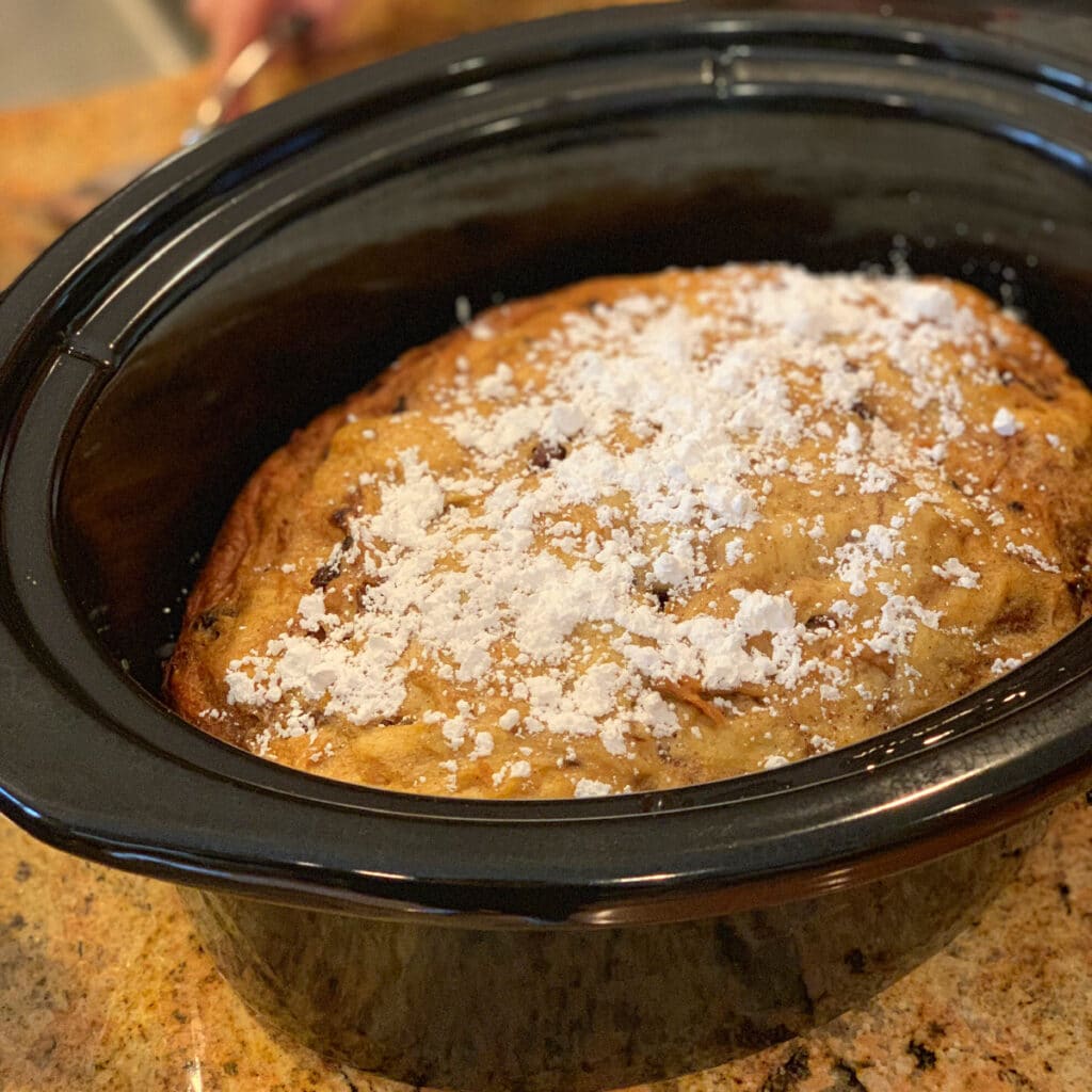 Top view of finished french toast in a a black oval crockpot pot sprinkled with powdered sugar
