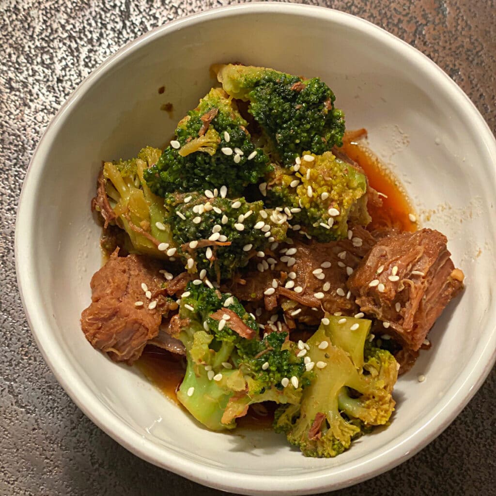 Top view of a bowl containing chucks of beef green veggies and sesame seeds