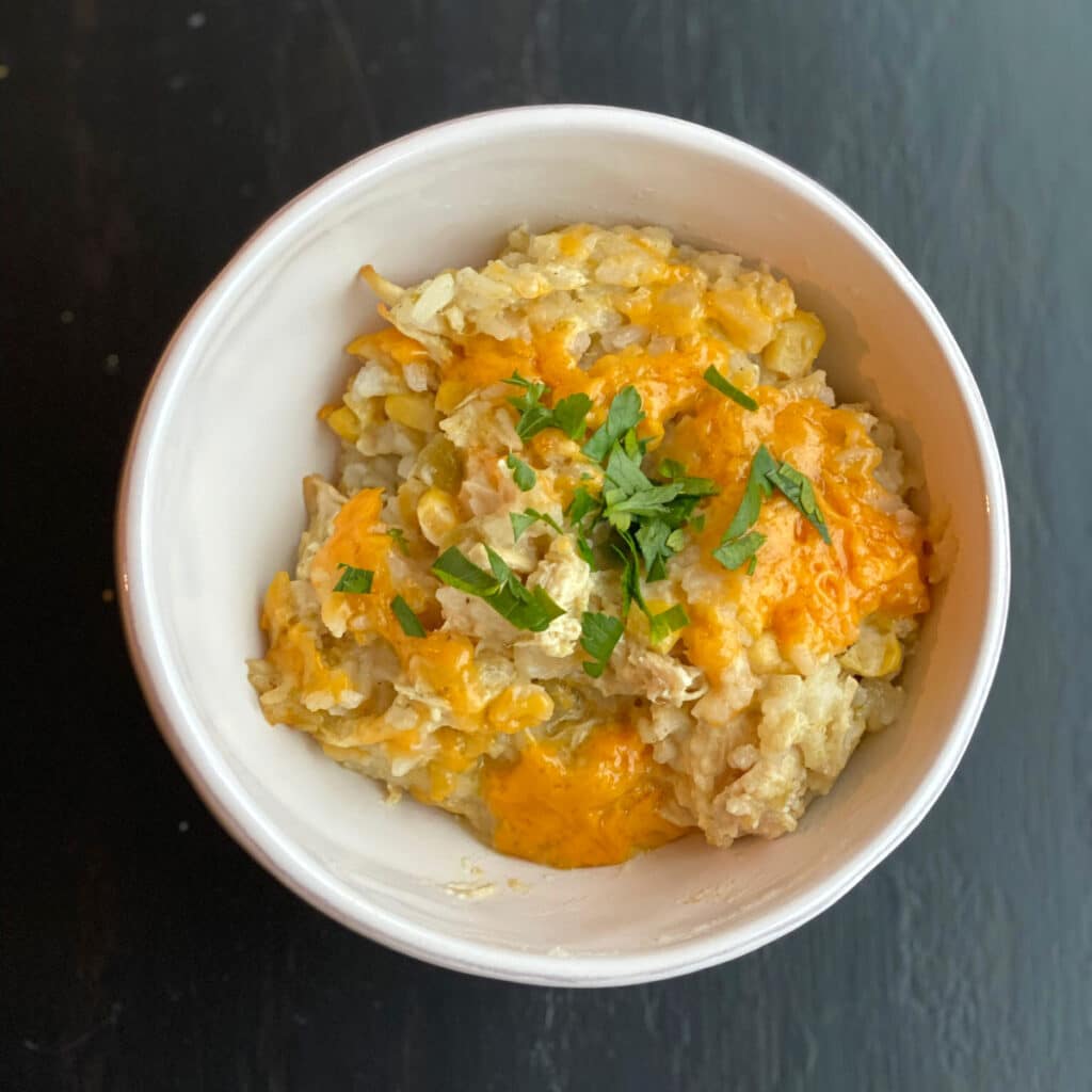 Looking down into a round white bowl containing melted cheese chicken and rice.  