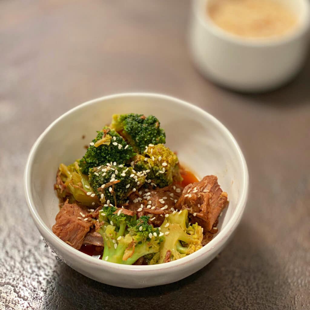 Broccoli, beef and sesame seed in a round white bowl