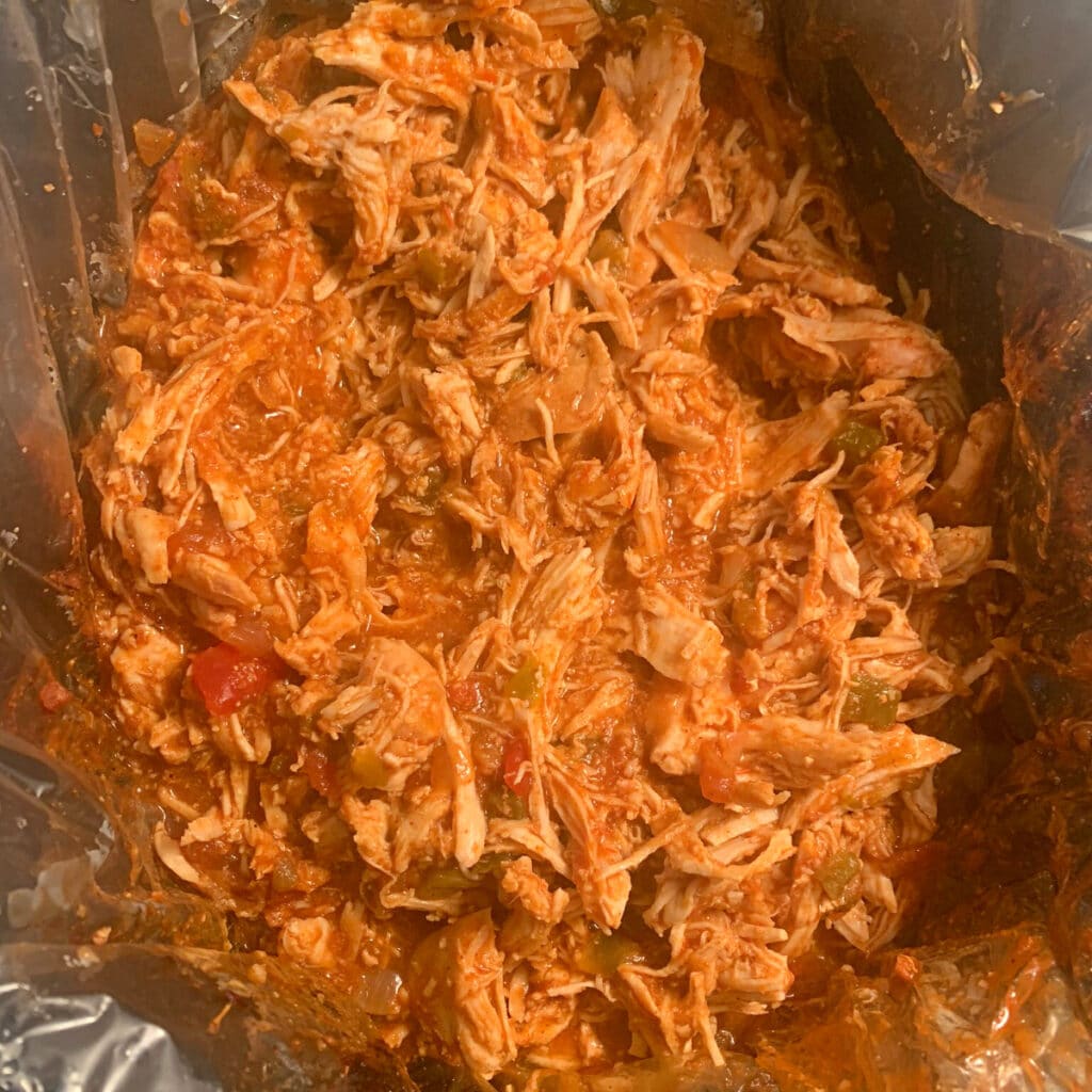 Looking down into a crockpot filled with shredded chicken and seasonings, cooked