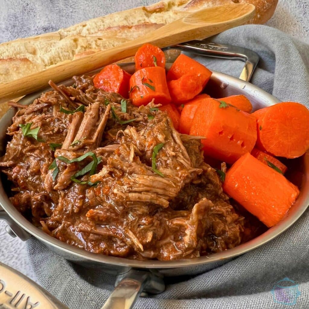 Slow cooker Balsamic roast in a metal dish with carrots and a French loaf
