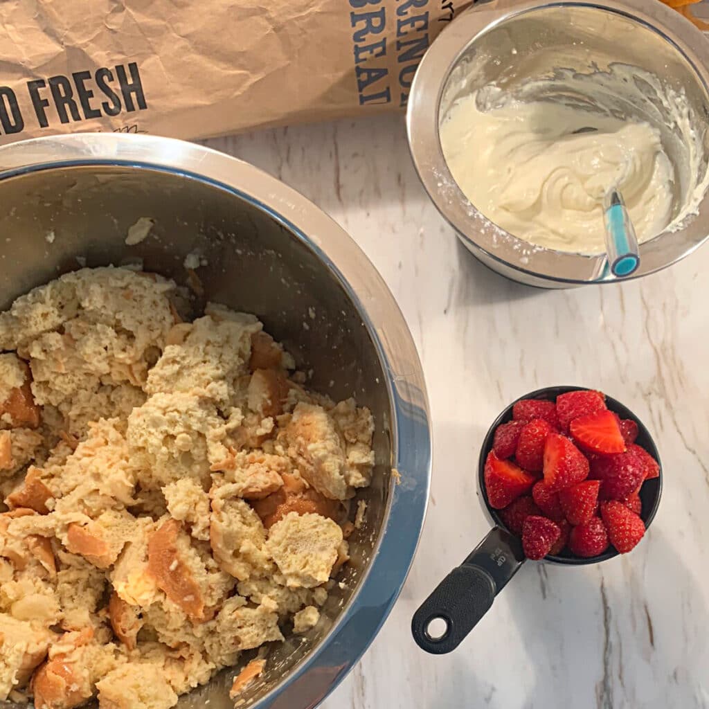 a bowl of soaked French bread, a cup of fresh strawberries and a bowl of cream cheese mixture