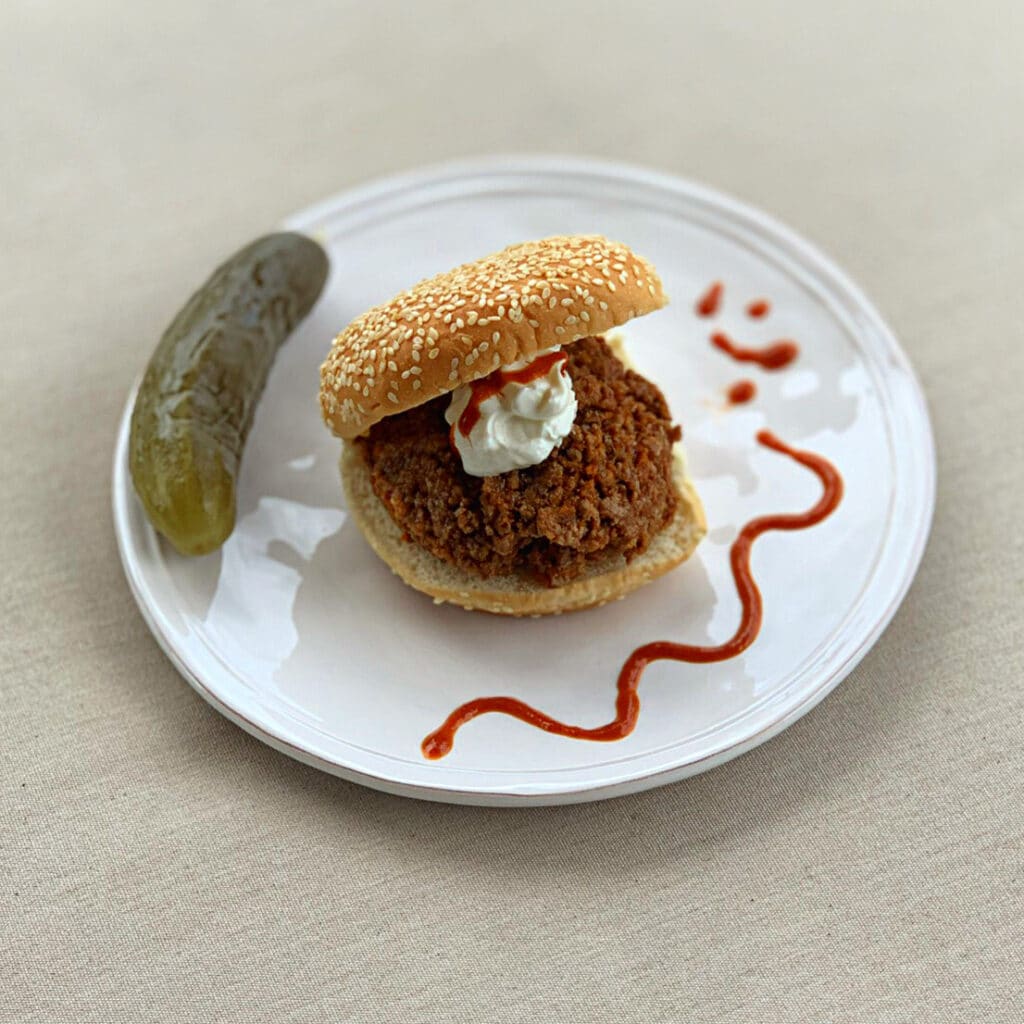 close up of slow cooker sloppy taco Joe on a round sesame bun topped with sour cream and decorated with hot sauce