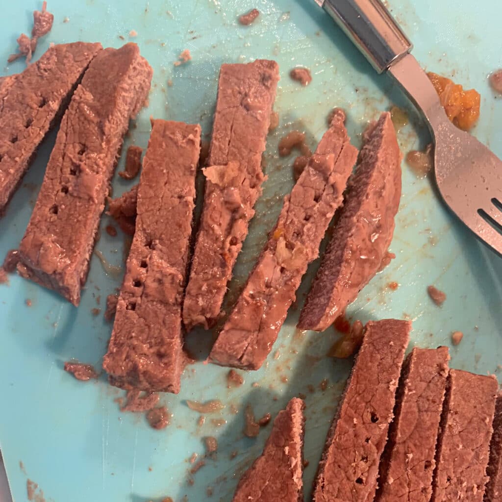 beef strips on a cutting board with a fork in the background