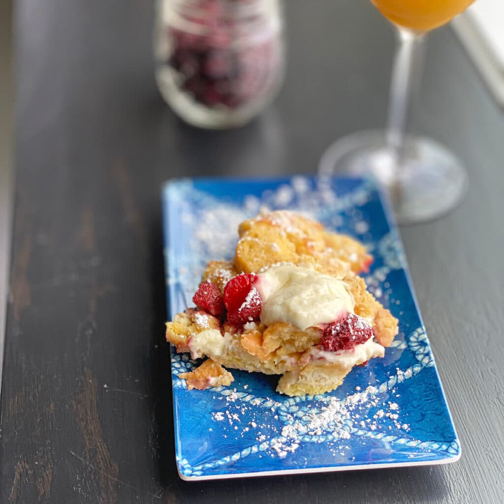 finished French Toast on a blue plate with orange juice and topping blurred in the backgroun