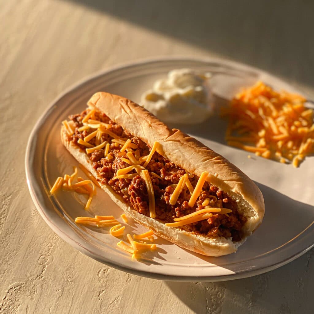 finished sandwich on a round white plate with sour cream and shredded cheese in the background 