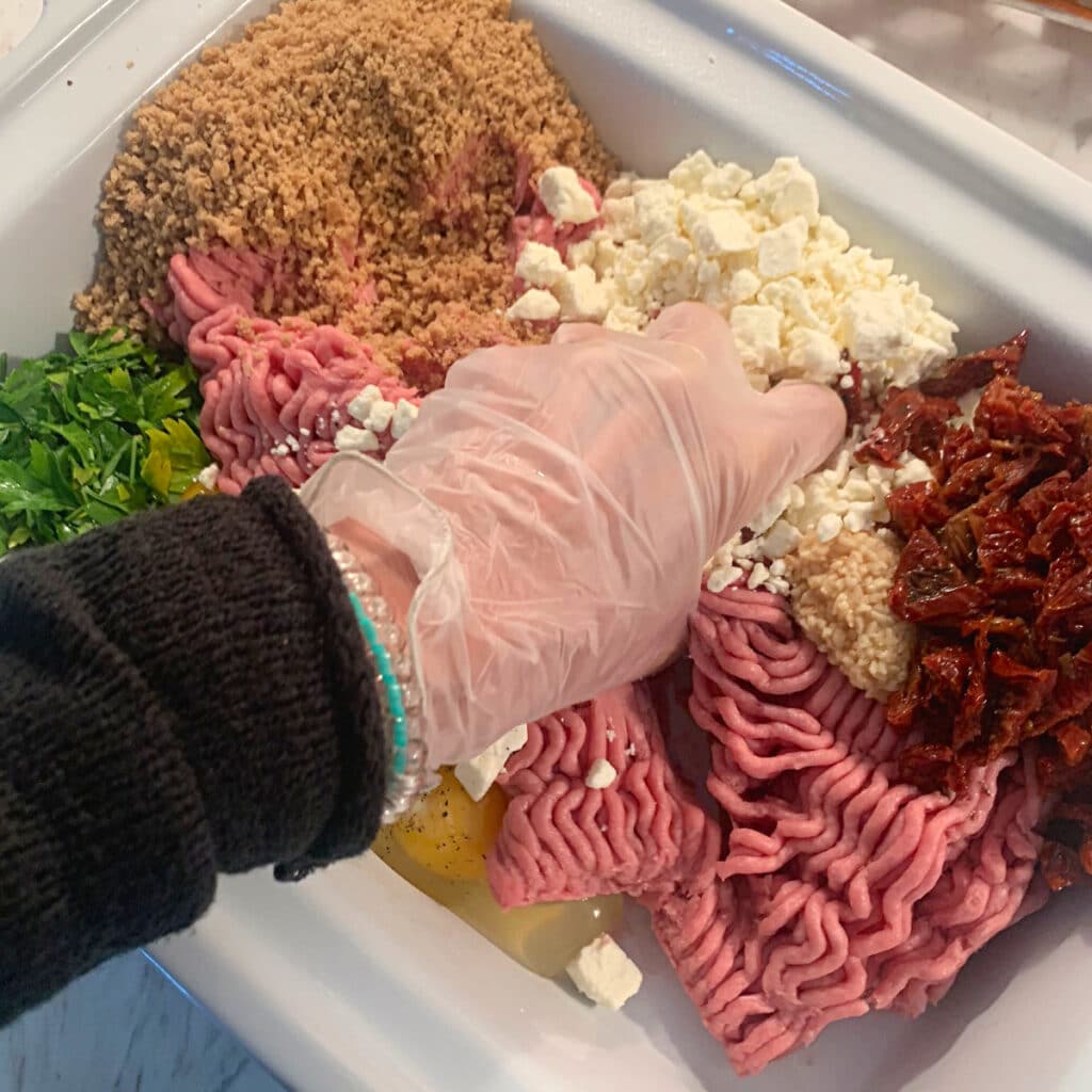 All turkey meatloaf ingredients in slow cooker with a gloved hand mixing them