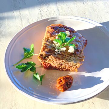Corner piece of meatloaf on a round white plate in the afternoon sun
