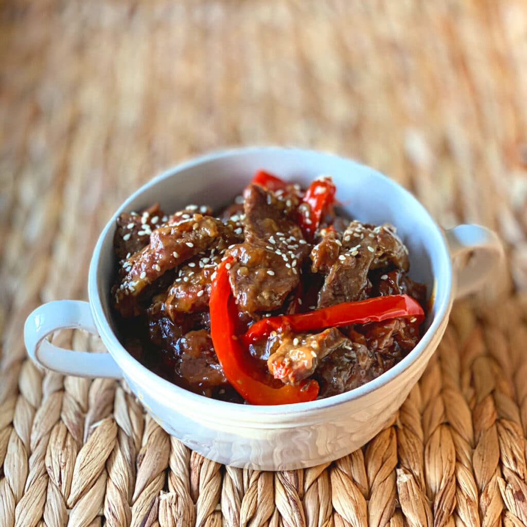 finished Mongolian Beef in a round white bowl with handles on a wicker mat