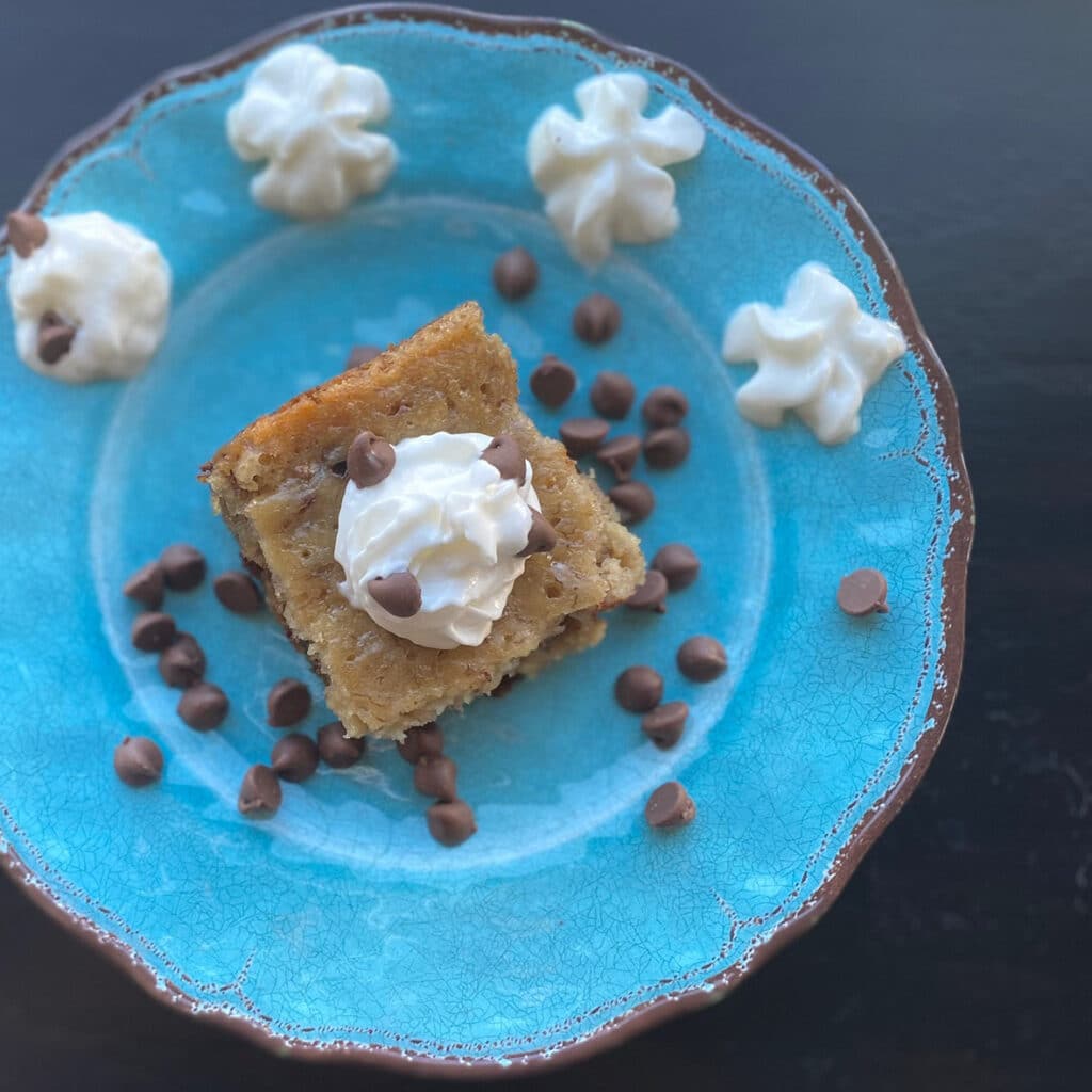 top view of brownie brownies on a blue plate with chocolate chips sprinkled around a dollop of whipped topping