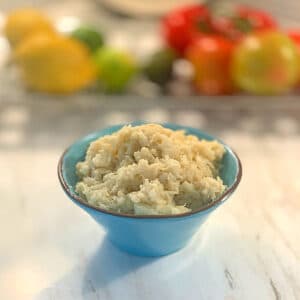 close up of a blue bowl filled with mashed cauliflower with a fruit tray in the backgroun