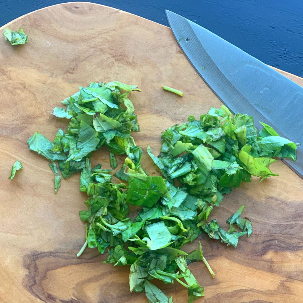 freshly chopped basil on a wood cutting board with a knife