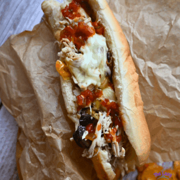 chicken cheesesteak sandwich with toppings on a wooden board