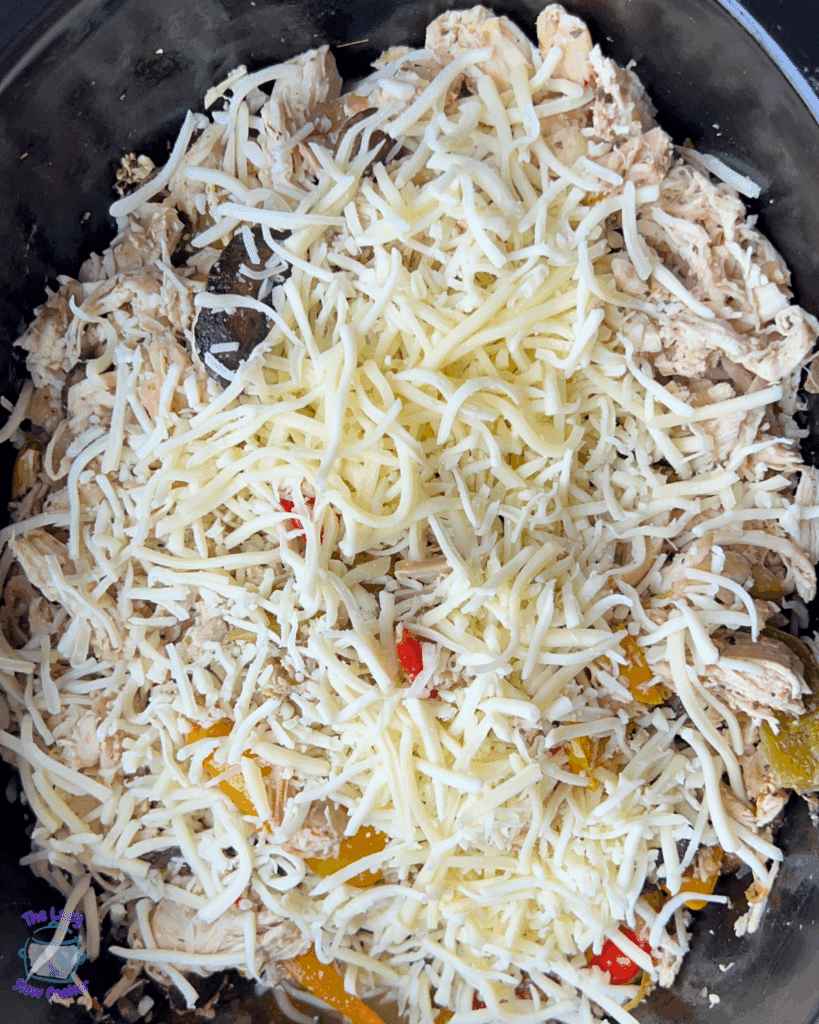 All chicken cheesesteak ingredients in a greased slow cooker before melting cheese