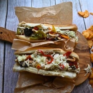 two chicken cheesesteaks with toppings on a wooden board