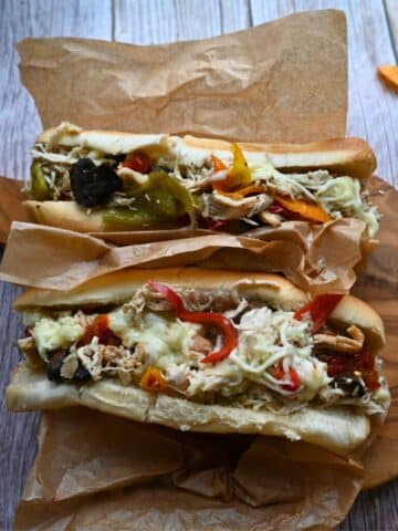 two chicken cheesesteaks with toppings on a wooden board