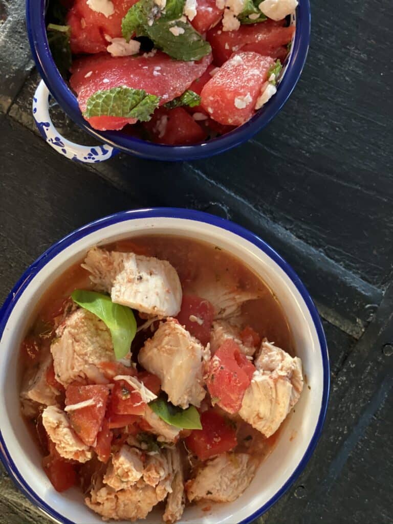 a bowl of chicken with tomatoes and basil in a light broth