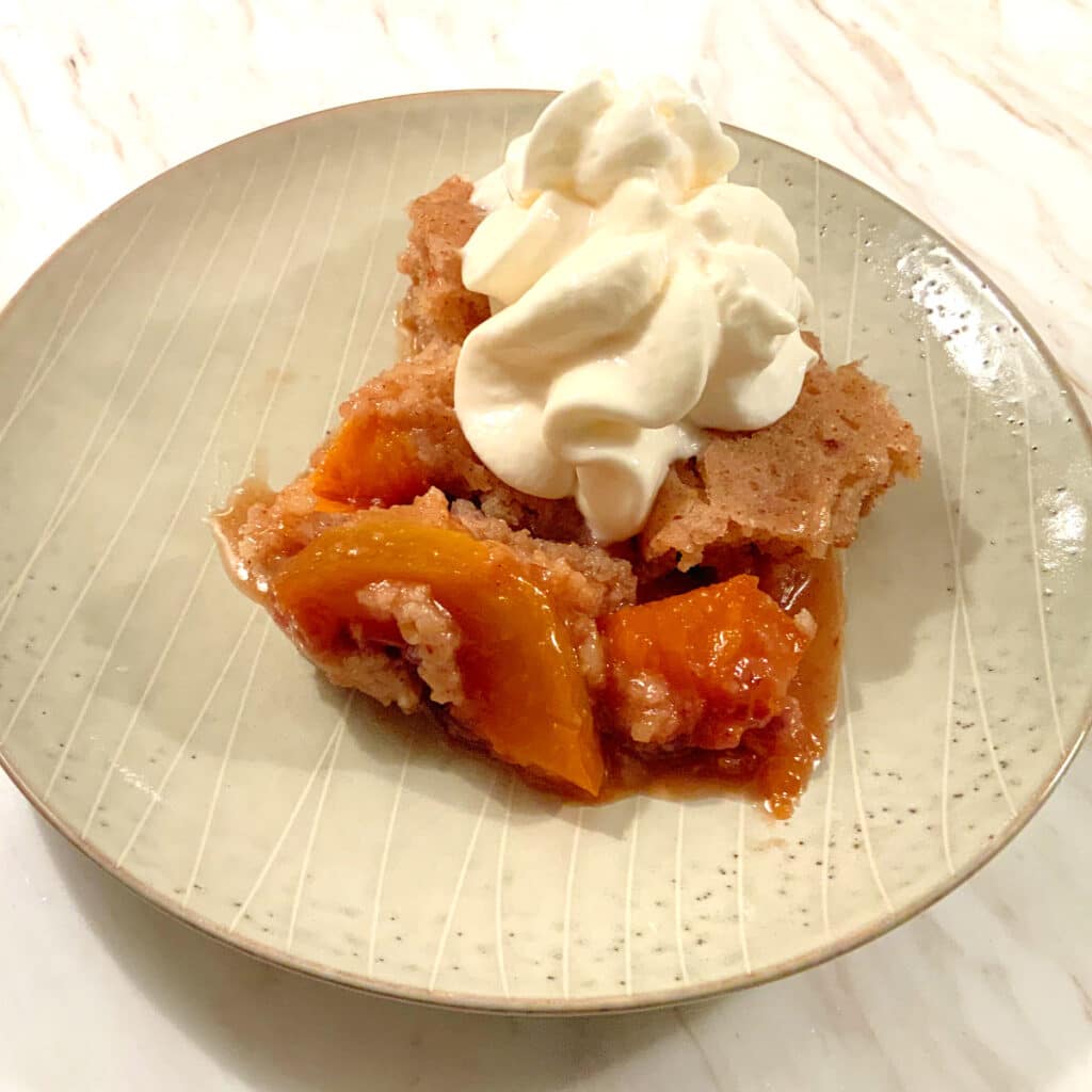 finished peach cobbler on plate with whipped cream on top