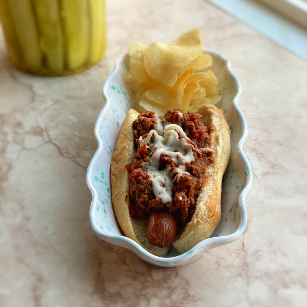 Hot dog covered with chili on an oval plate with potato chips 