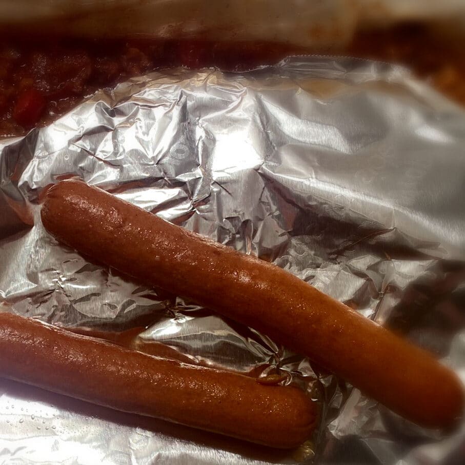 Top view of a crockpot with chili covered in foil with two hot dogs on top