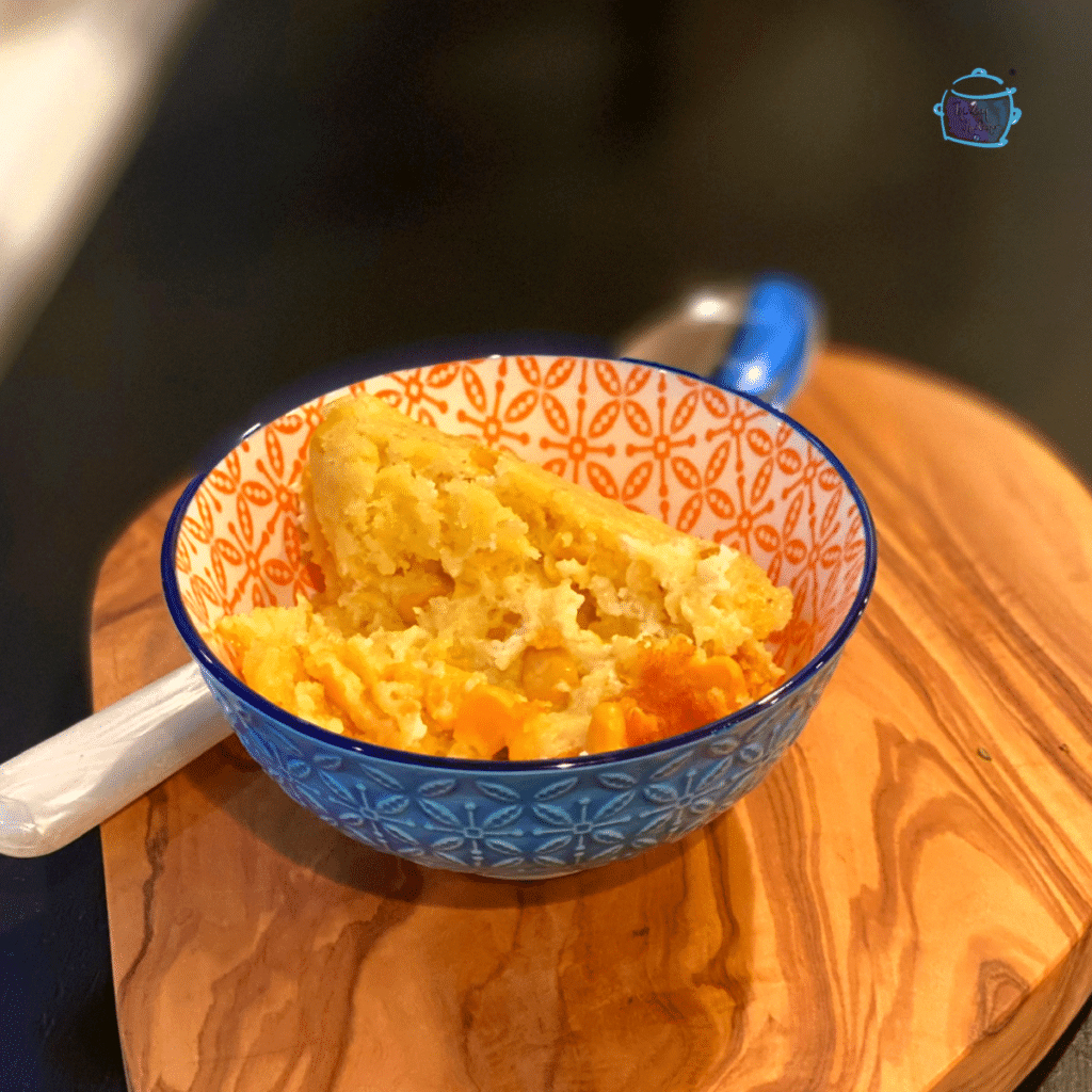 Slow cooker corn spoon bread in a blue bowl with a spoon behind it