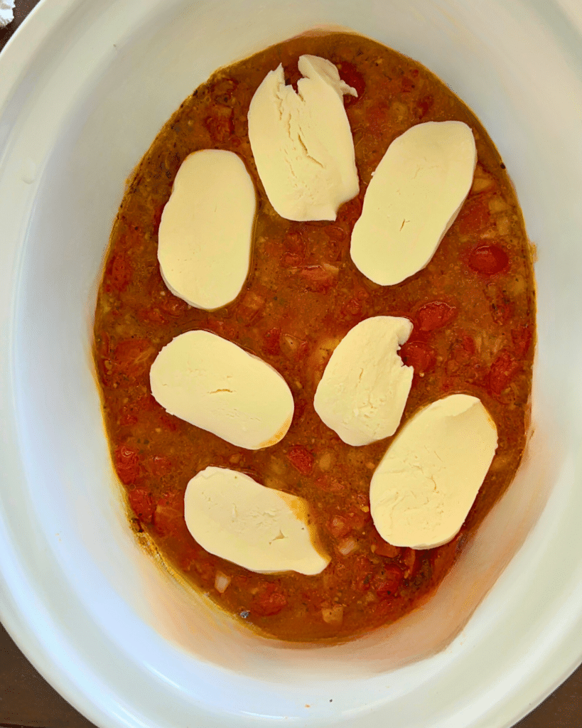chicken in crockpot with cheese slices before cheese is melted