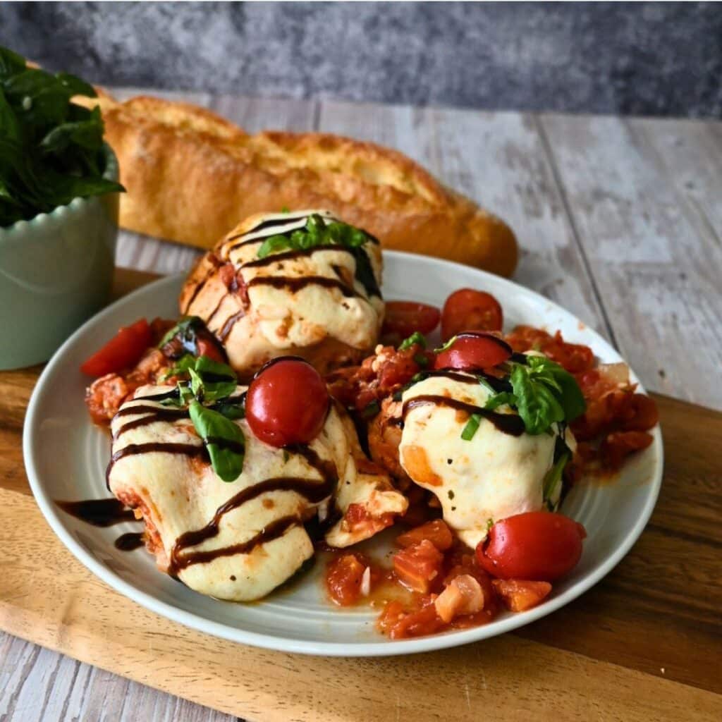 A plate of caprese chicken ready to serve with bread in the background