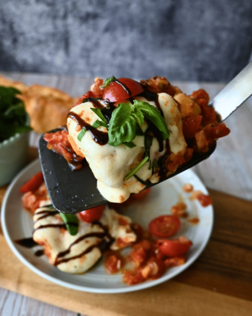 slow cooker Caprese chicken on a spatula over a plate of the same