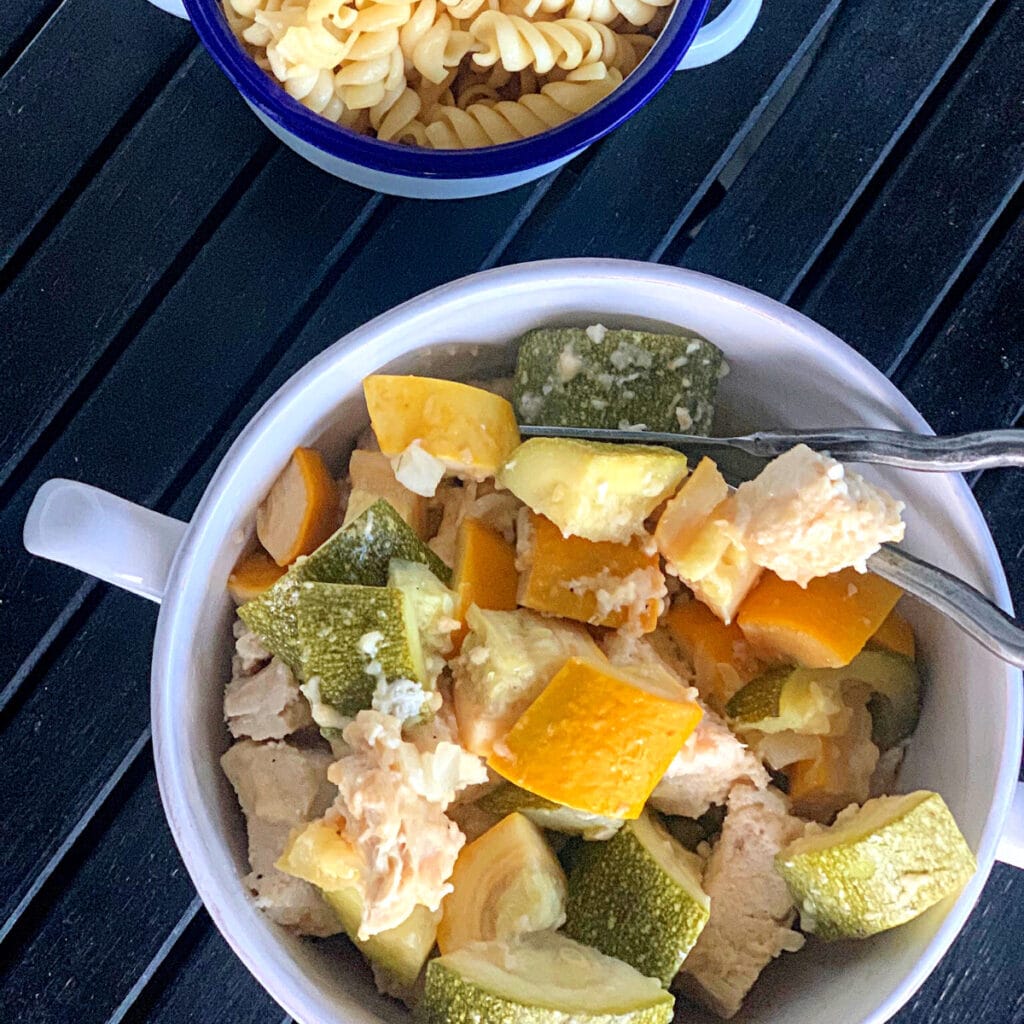 Top view of Zucchini and squash parmesan with chicken and a bowl of pasta in the background, 