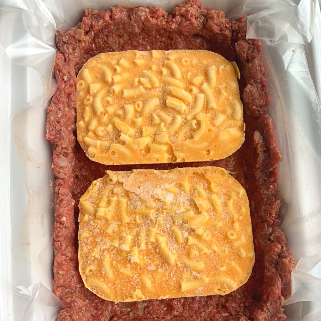 meatloaf in pan on bottom and up walls of slow cooker with two small frozen mac and cheese blocks in the middle