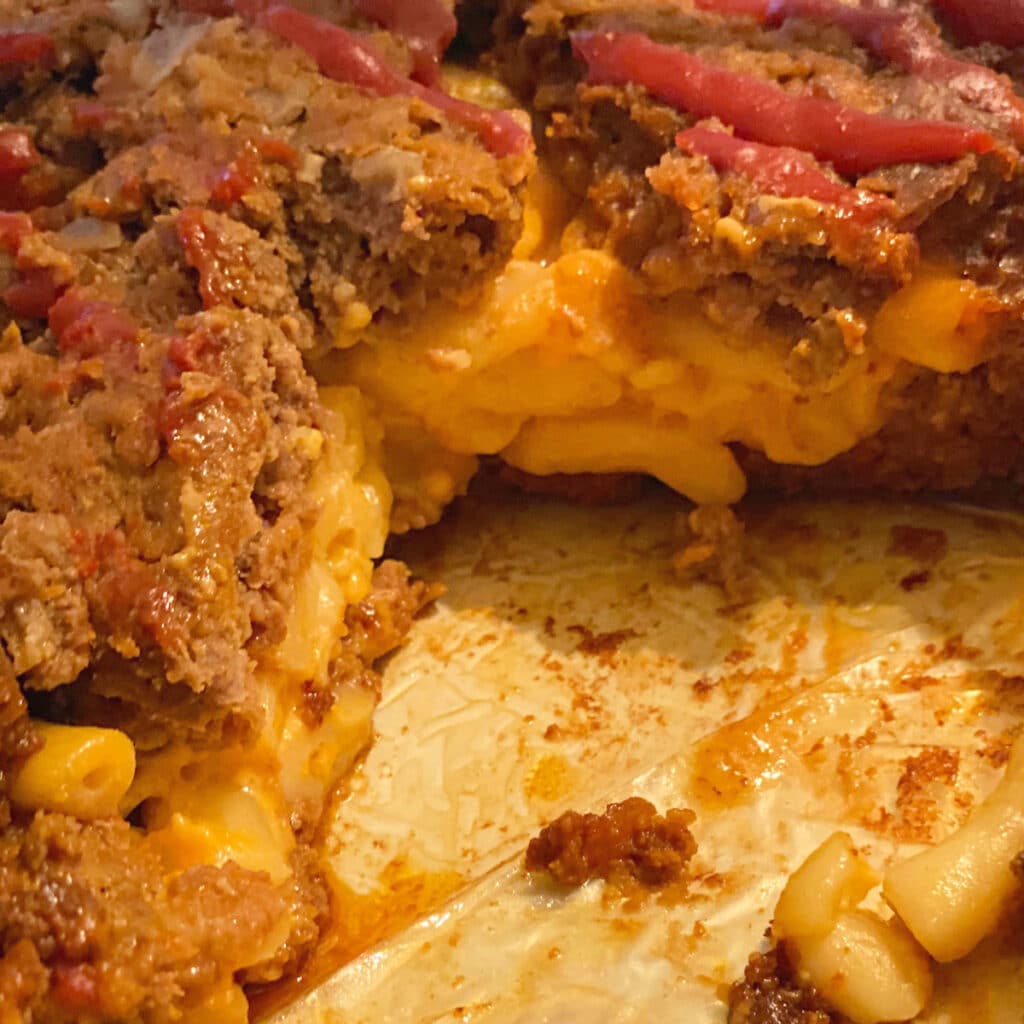 close up of macaroni and cheese surrounded by meatloaf still iln the pan with a piece missing