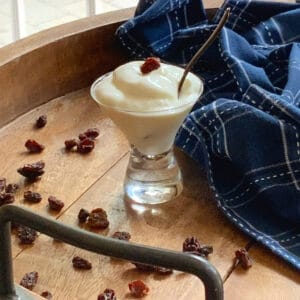 close up photo of finished greek yogurt in a small glass with raisins all around and one raisin on top and a spoon