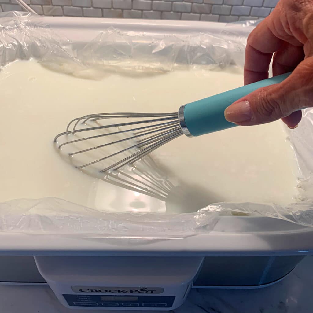 white casserole crockpot with a blue whisk mixing milk and yogurt