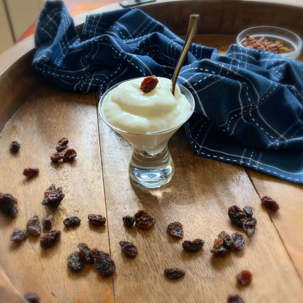 a shot of finished yogurt with raisins, granola and a blue dish towel for decoration