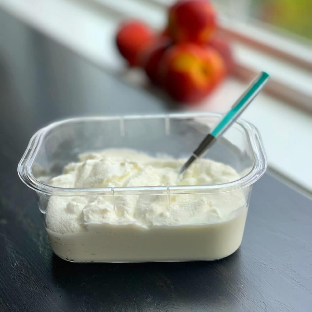 yogurt in a plastic container with peaches in the background