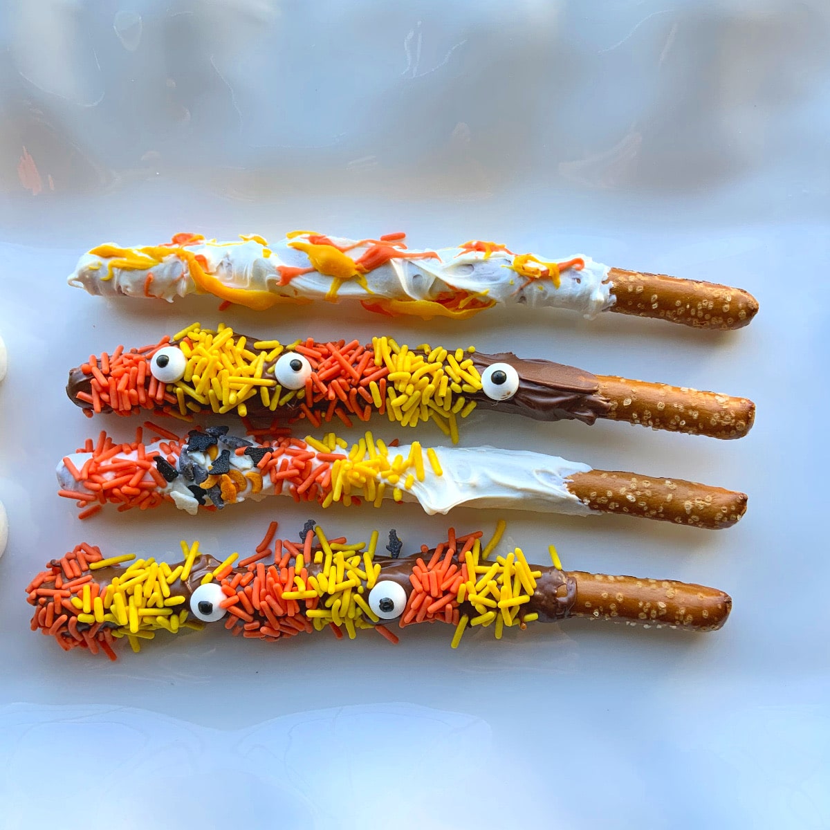 4 pretzel rods covered in melting chocolate, orange and yellow sprinkles and candy eyes