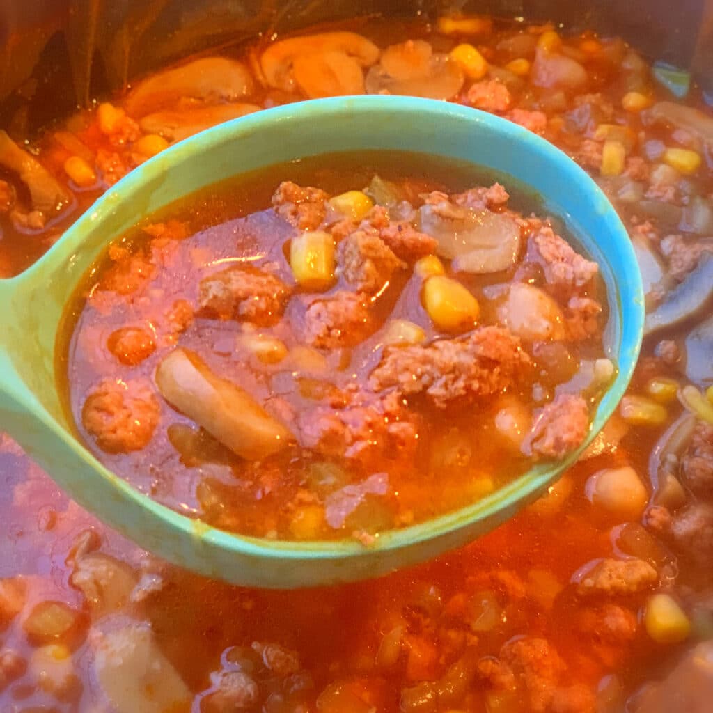 Close up of turkey burger soup in a blue laden held over the crockpot full of soup