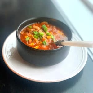 View of soup from the side in a round black bowl with a white handled spoon sticking out of it,