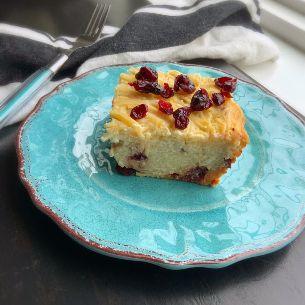 side view of piece of kugel cut from the whole on a turquoise plate with a fork in the background