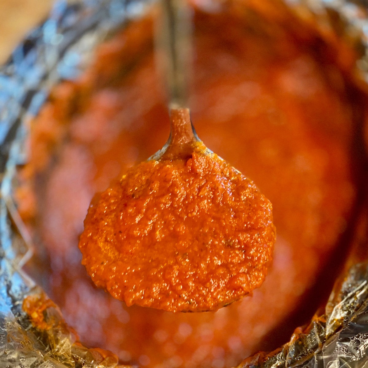 Close up of a ladle filled with marinara with a crock of marana blurred in the background