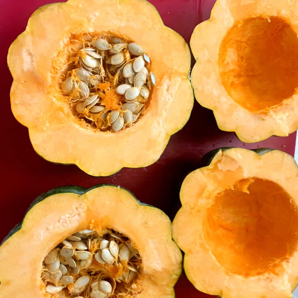 Four halves of acorn squash raw. Two have seeds cleaned out and two don’t.