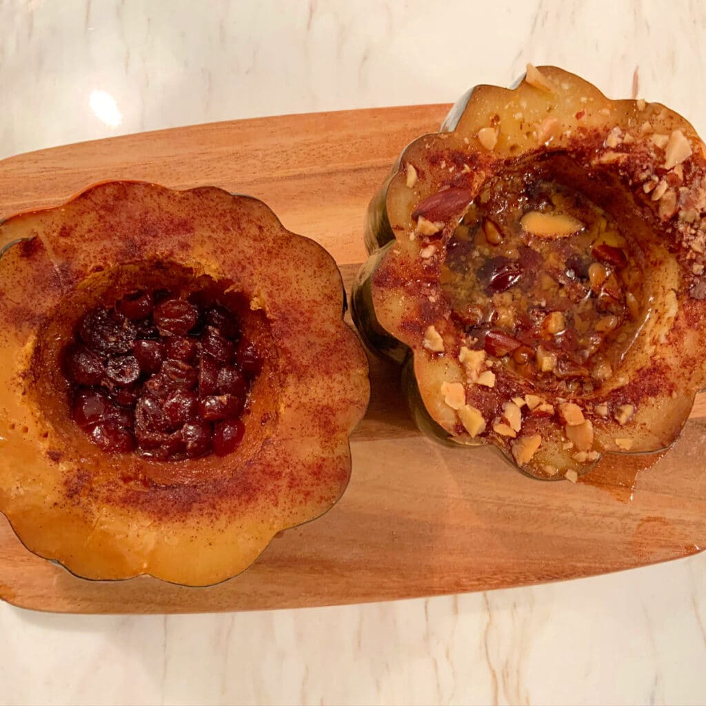 Looking down on two halves of cooked acorn squash one filled with dried cranberries and then other with cinnamon , butter and crushed almonds