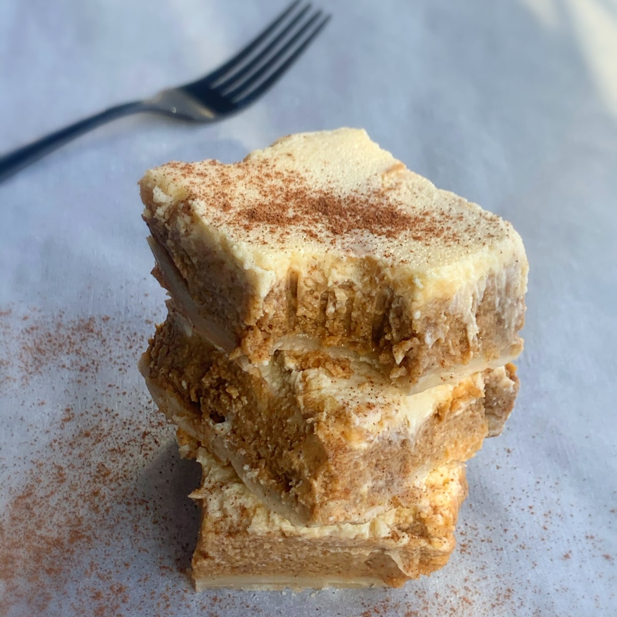 stack of pumpkin cheesecake bars with a black for blurred in the bakcground