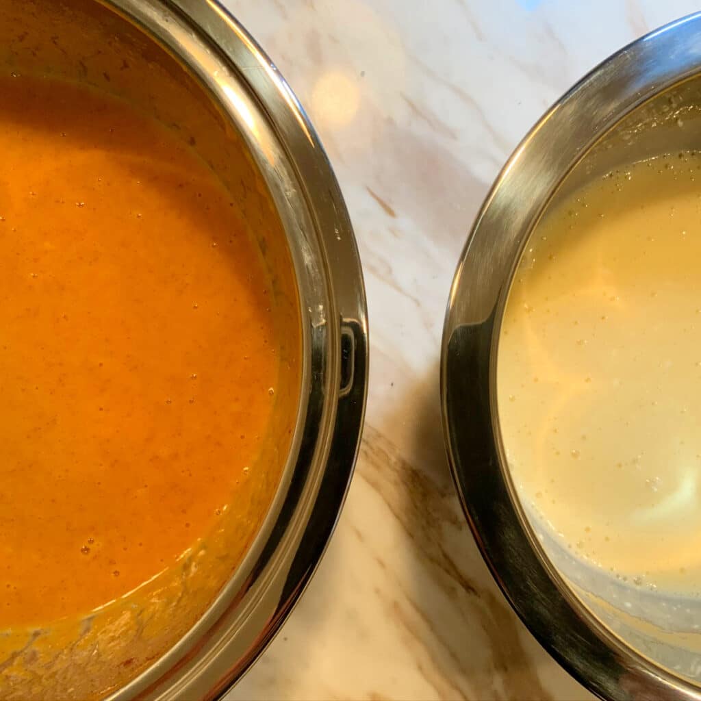 close up of two mixing bowls. one with mixed ingredients for pumpkin layer the other with mixed ingredients of cheesecake layer