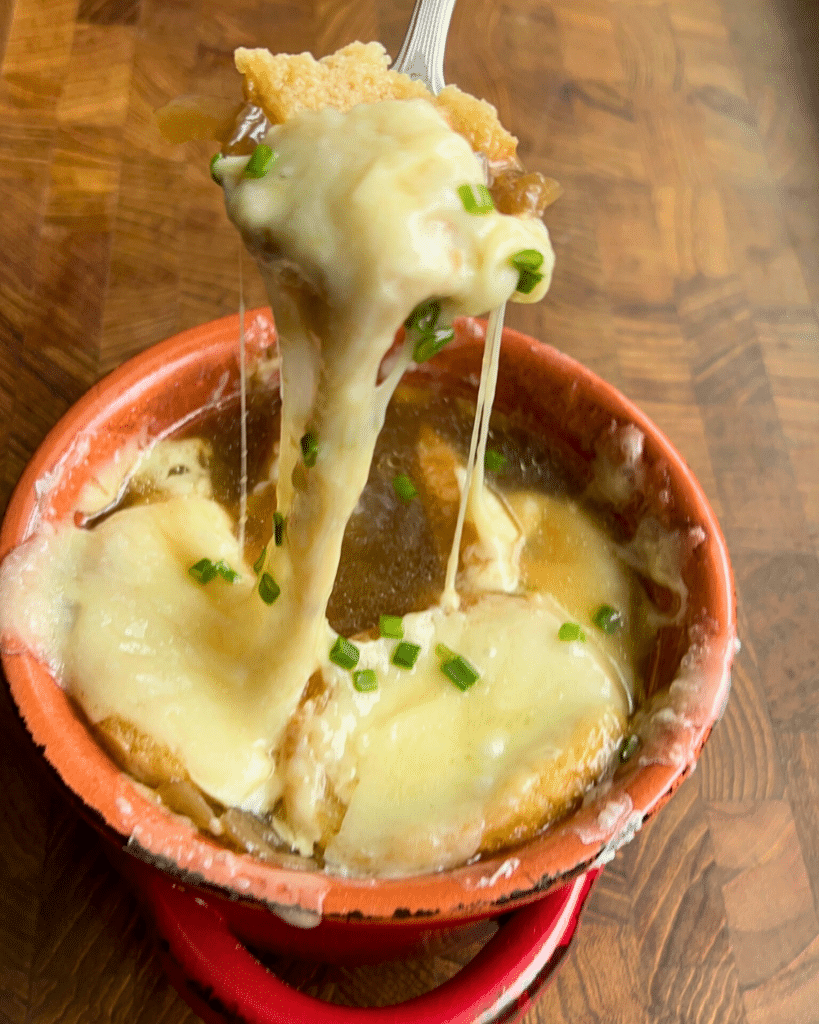 A bowl of french onion soups with a spoon pulling up some of the gooey cheese topping