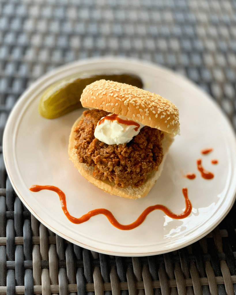 Sloppy Taco on a round roll topped with cheese and a dollop in sour cream in the background