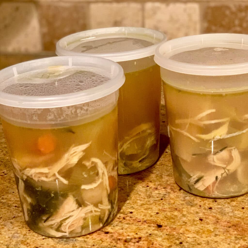 three storage containers with chicken soup ready on a counter top. ready for the freezer